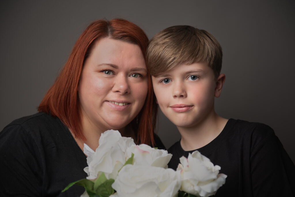 Portrait photograph of a mother and son smiling and holding a bunch of flowers